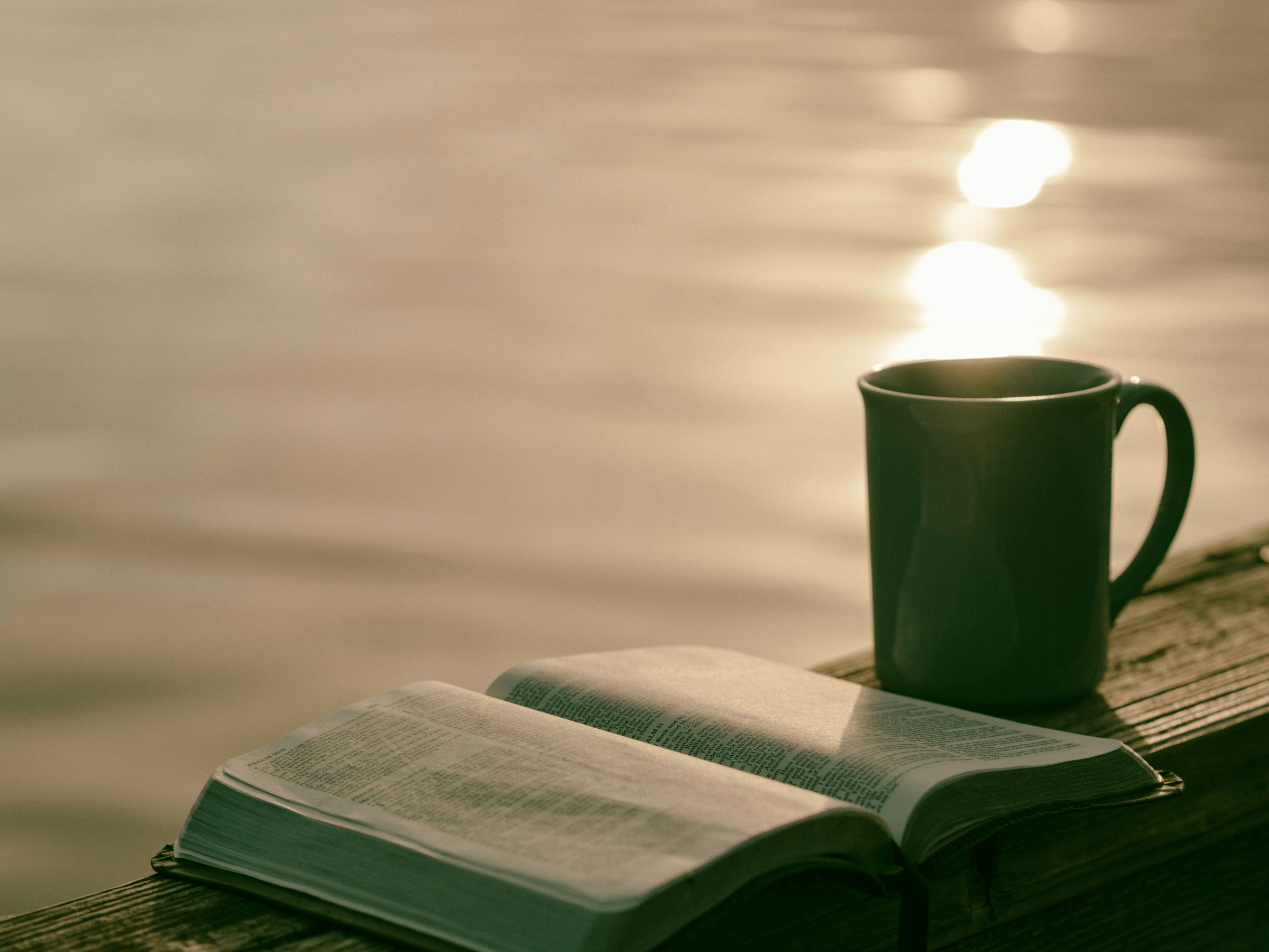 Green ceramic mug beside the Bible by water